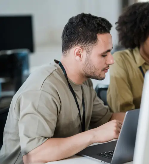 A trainee working on his laptop with an instructor.